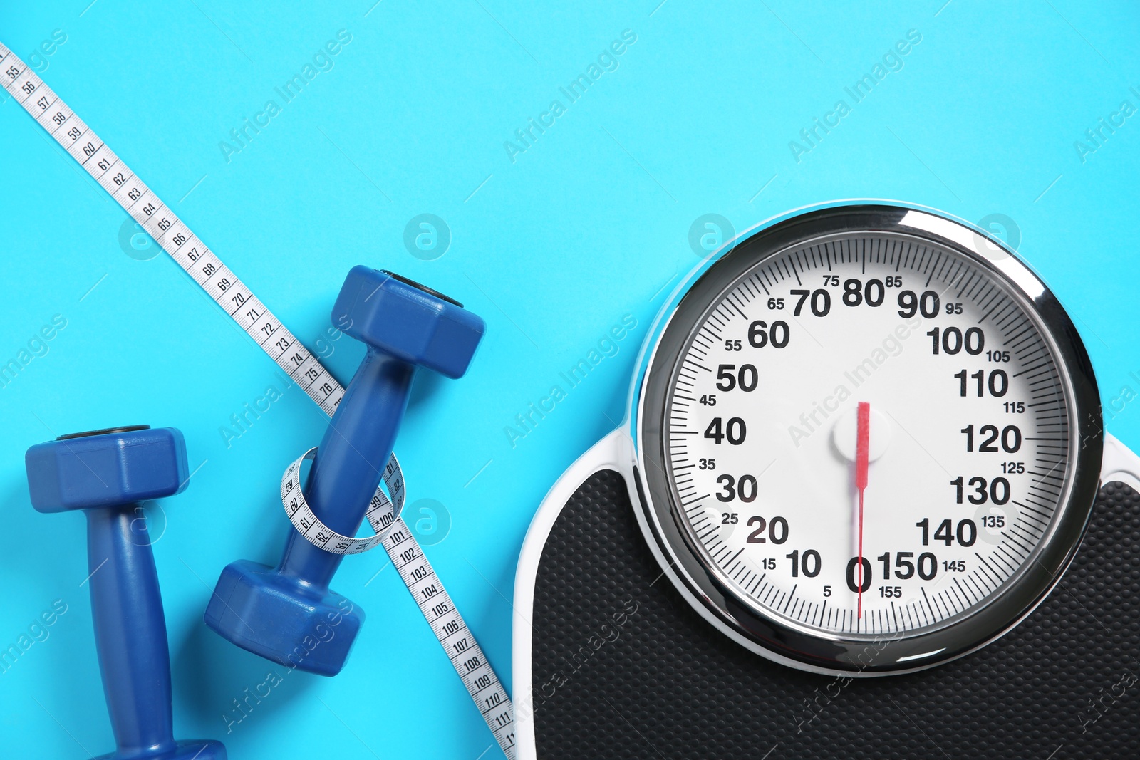 Photo of Scale, dumbbells and measuring tape on light blue background, flat lay