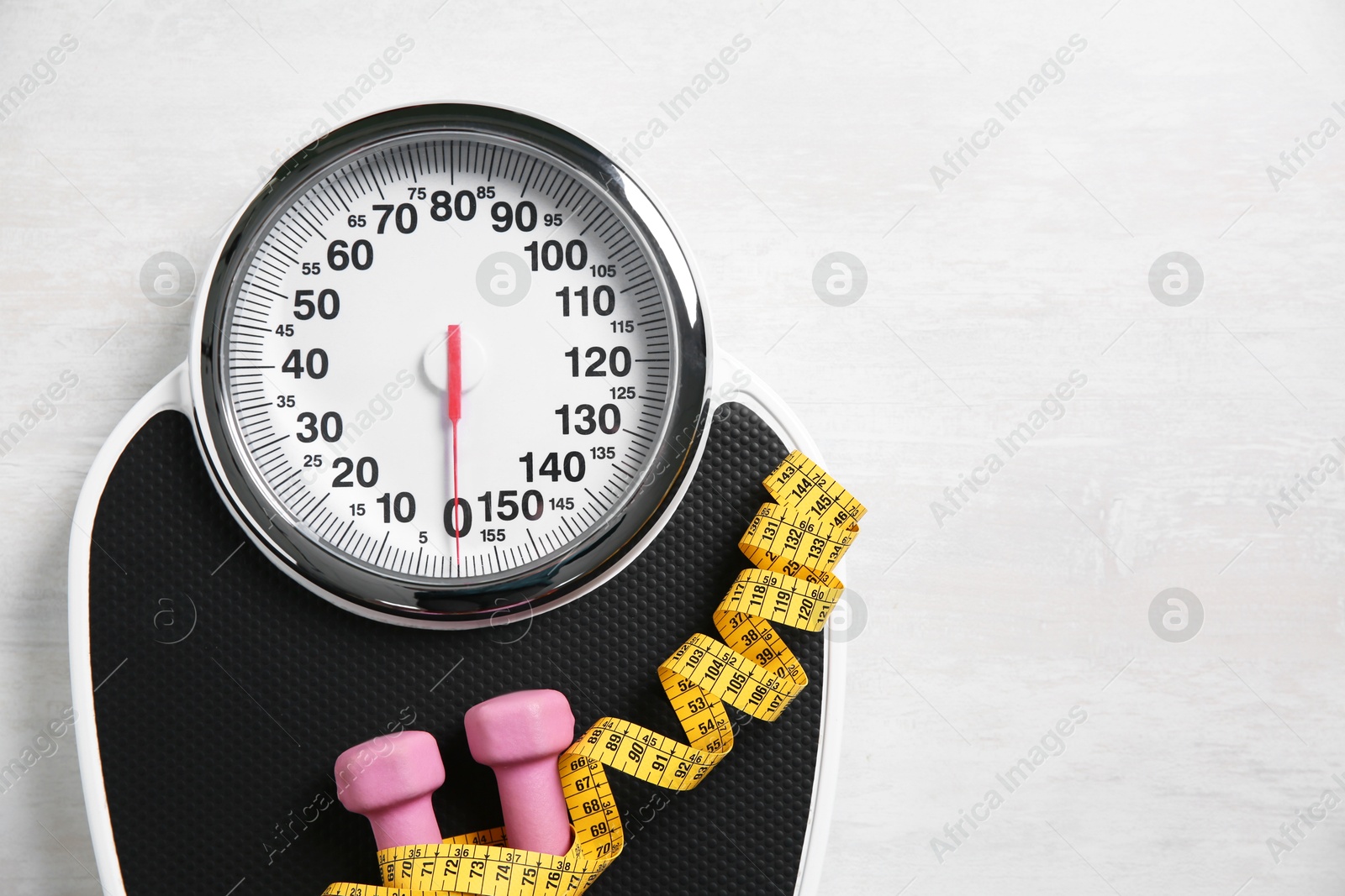 Photo of Scale, dumbbells and measuring tape on white wooden background, top view. Space for text