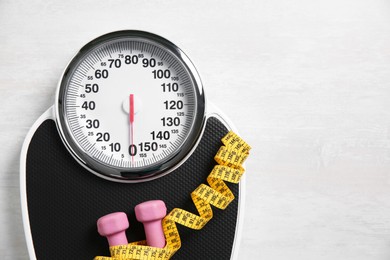 Photo of Scale, dumbbells and measuring tape on white wooden background, top view. Space for text