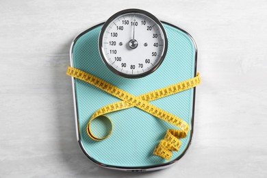 Photo of Scale tied with measuring tape on light wooden background, top view