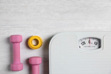 Photo of Bathroom scale, measuring tape and dumbbells on white wooden background, flat lay. Space for text