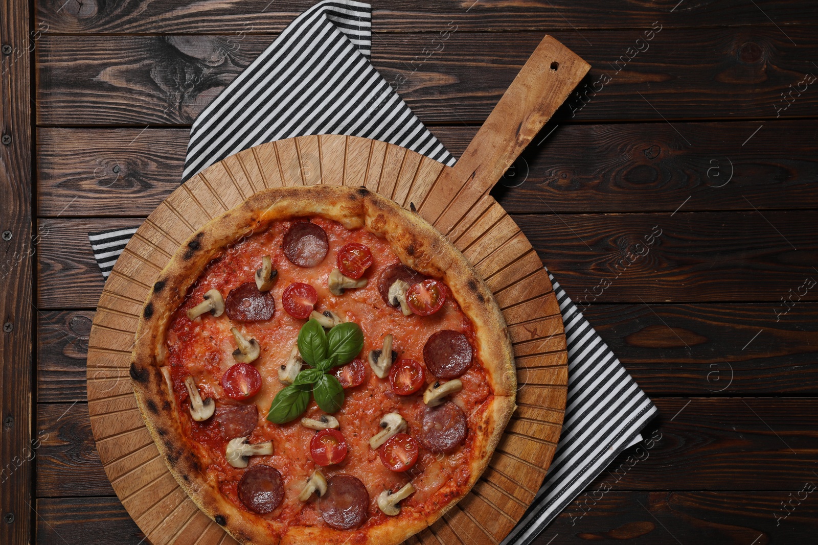 Photo of Delicious pizza with tomatoes, salami, mushrooms and basil on wooden table, top view