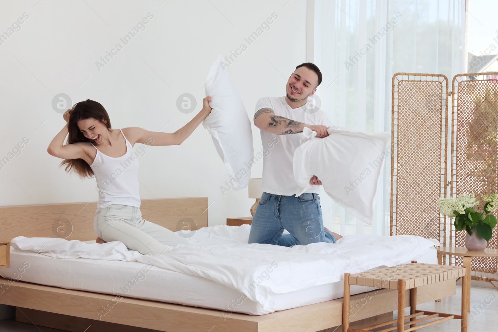 Photo of Happy couple having pillow fight on bed at home