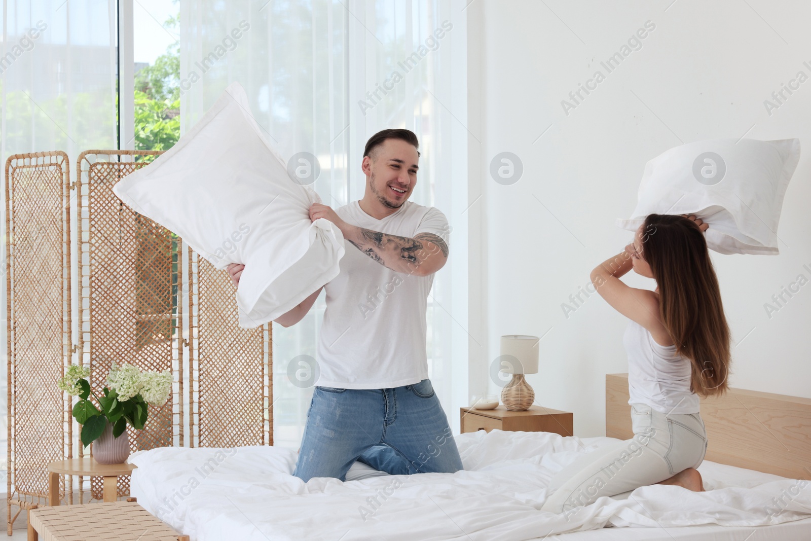 Photo of Happy couple having pillow fight on bed at home