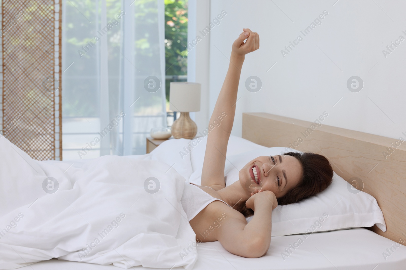 Photo of Bedtime. Happy woman lying in bed indoors