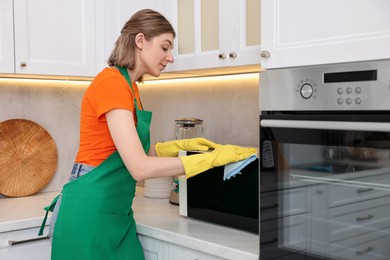 Photo of Professional janitor wearing uniform cleaning microwave oven in kitchen