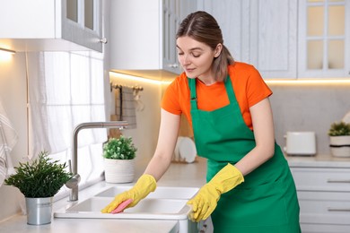 Photo of Professional janitor wearing uniform cleaning sink in kitchen