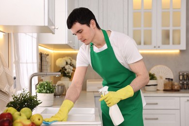 Photo of Professional janitor cleaning sink with rag and detergent in kitchen