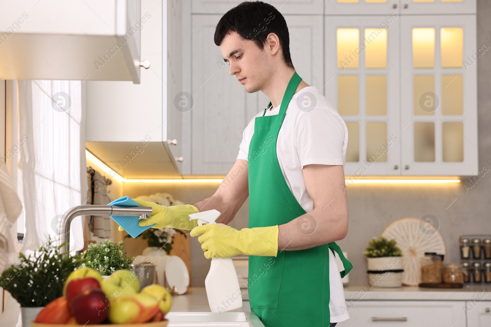 Photo of Professional janitor cleaning tap with rag and detergent in kitchen