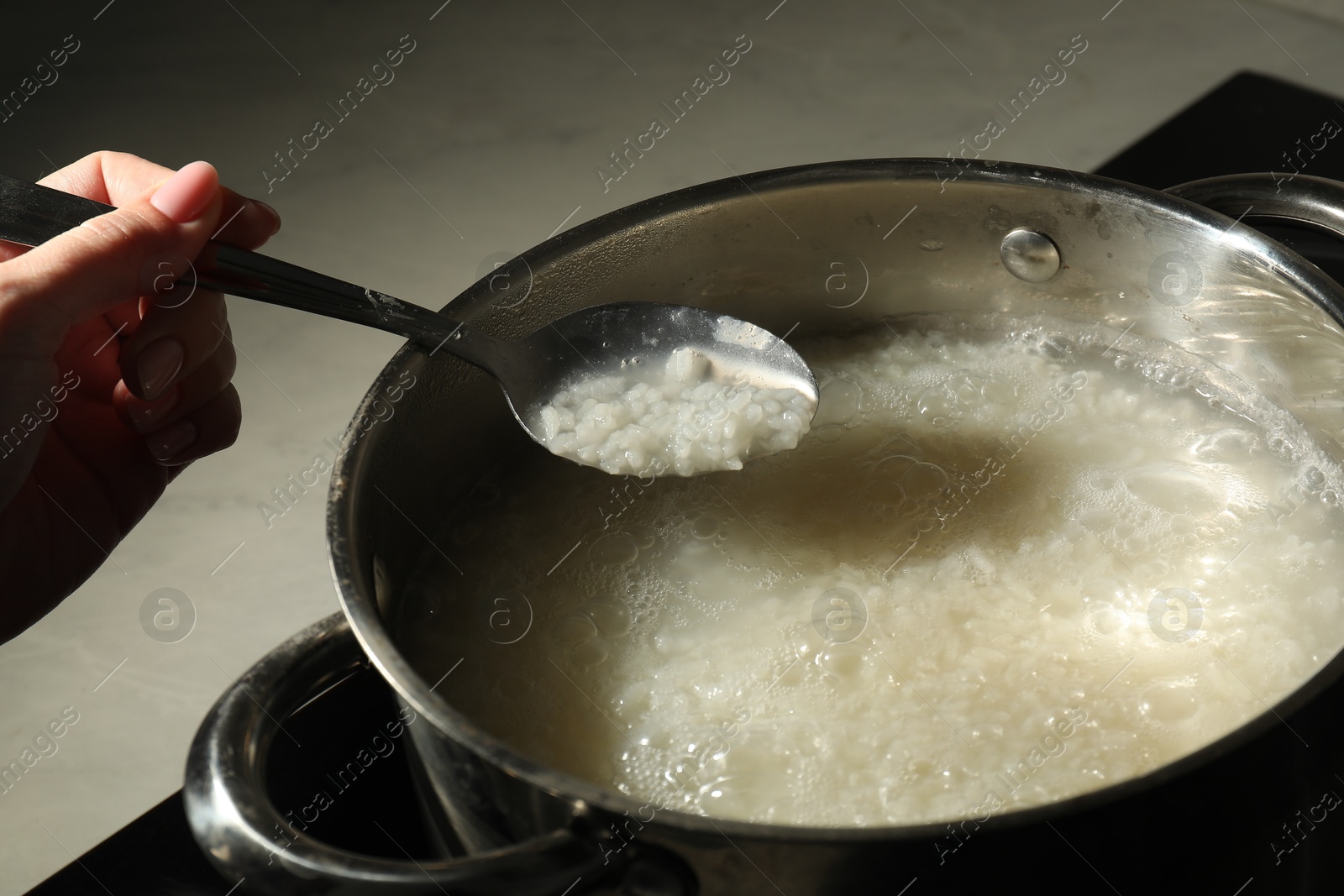 Photo of Woman holding spoon with boiled rice over pot, closeup