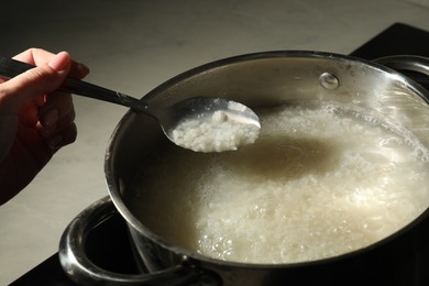 Photo of Woman holding spoon with boiled rice over pot, closeup