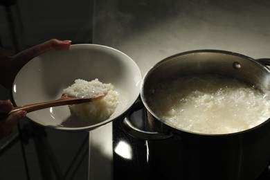 Photo of Woman putting boiled rice into bowl at countertop, closeup