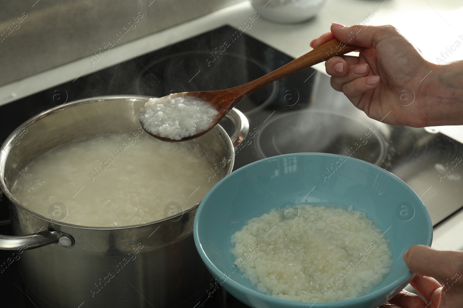 Photo of Woman putting boiled rice into bowl, closeup