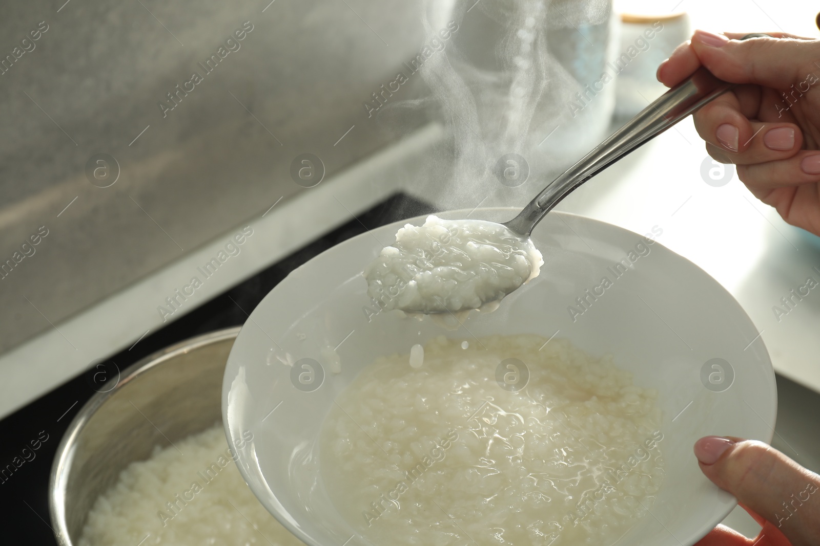 Photo of Woman putting boiled rice into bowl, closeup