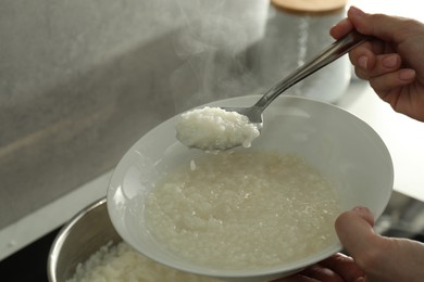 Photo of Woman putting boiled rice into bowl, closeup