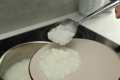 Photo of Woman putting boiled rice onto plate, closeup