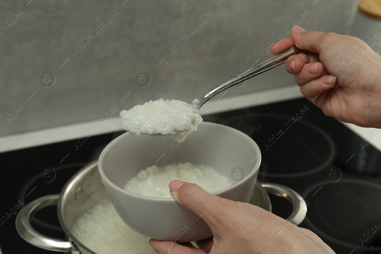 Photo of Woman putting boiled rice into bowl, closeup