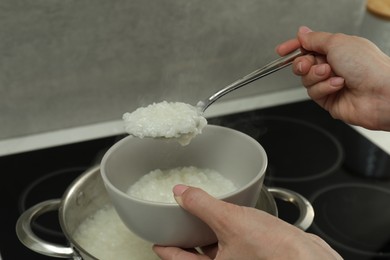 Photo of Woman putting boiled rice into bowl, closeup