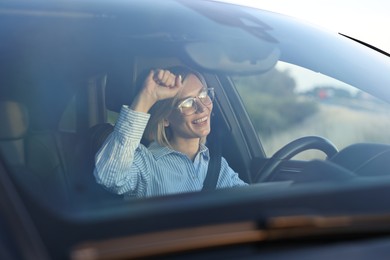 Photo of Smiling woman in glasses with seatbelt driving car, view through windshield
