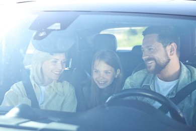 Photo of Happy family with cute daughter inside car together, view through windshield. Enjoying trip