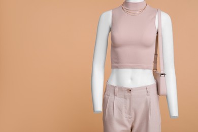 Photo of Female mannequin with bag dressed in stylish crop top and pants on beige background. Space for text