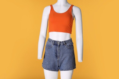 Female mannequin dressed in stylish tank top and denim shorts on orange background