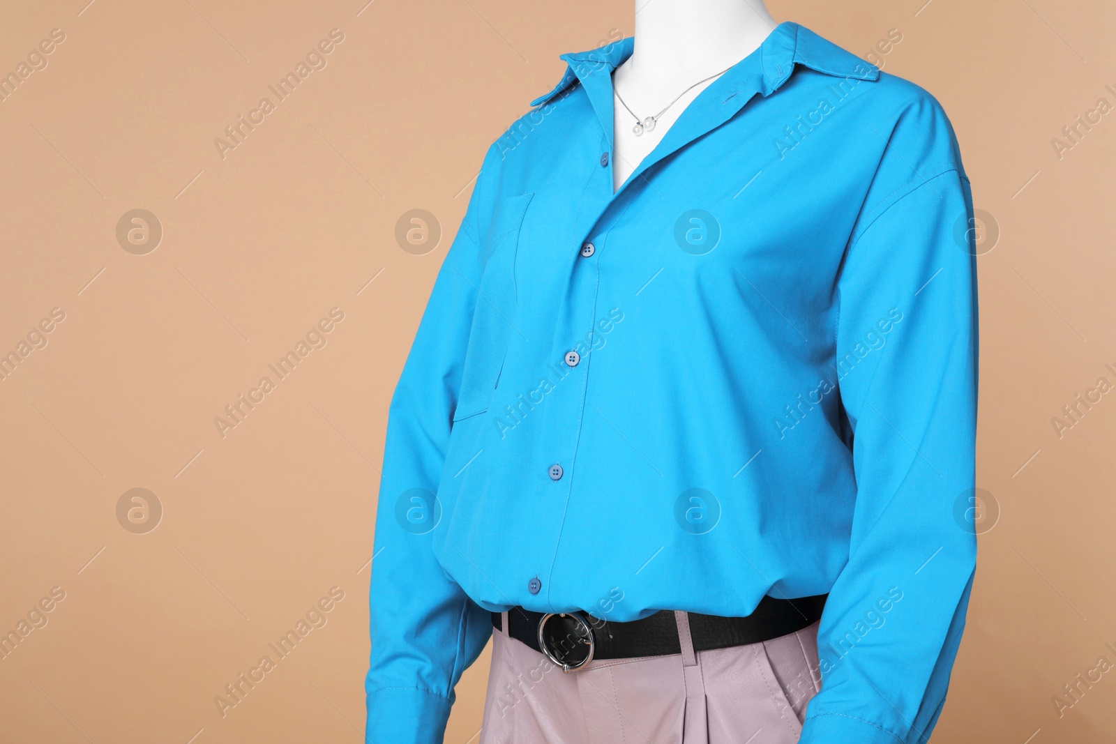 Photo of Female mannequin dressed in leather shorts and stylish light blue shirt with necklace on beige background, space for text