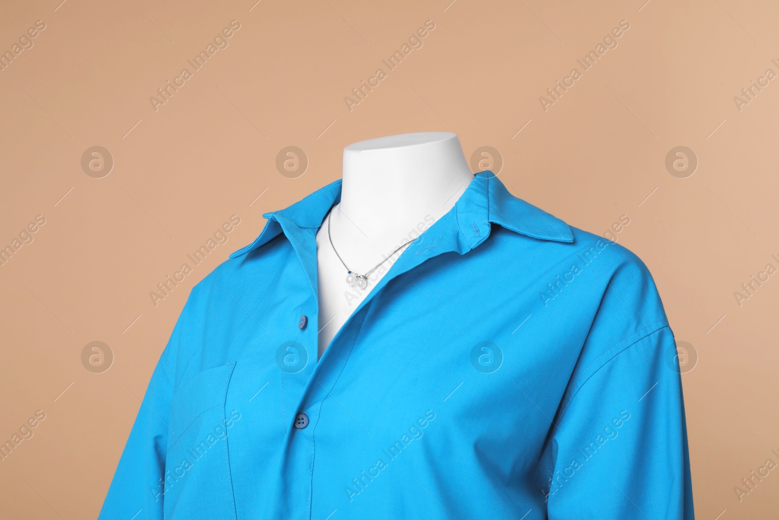 Photo of Female mannequin dressed in stylish light blue shirt with necklace on beige background