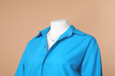 Photo of Female mannequin dressed in stylish light blue shirt with necklace on beige background