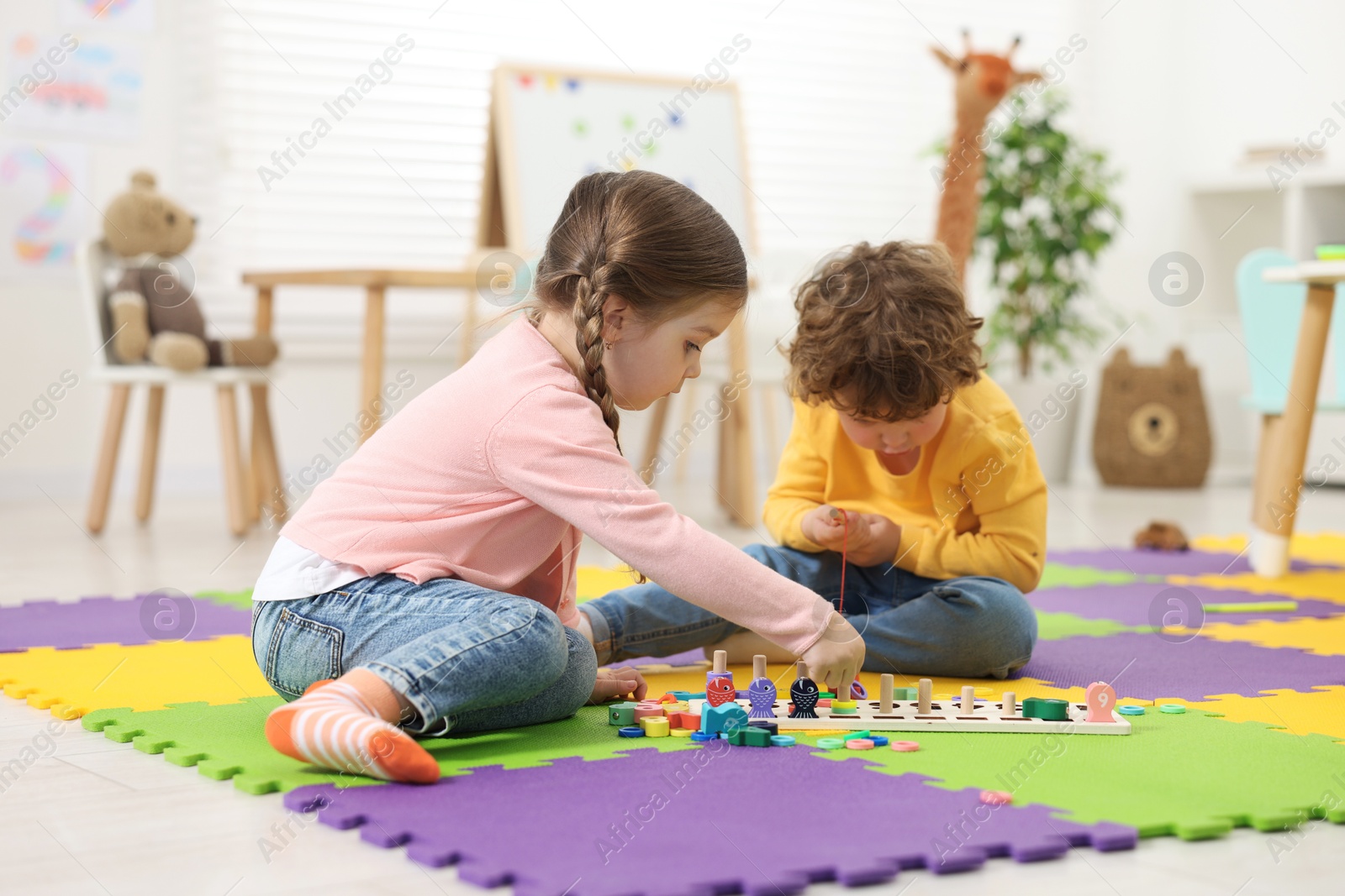 Photo of Cute little children playing with math game Fishing for Numbers on puzzle mat in kindergarten