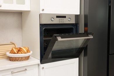 Photo of Open electric oven and croissants in kitchen. Cooking appliance