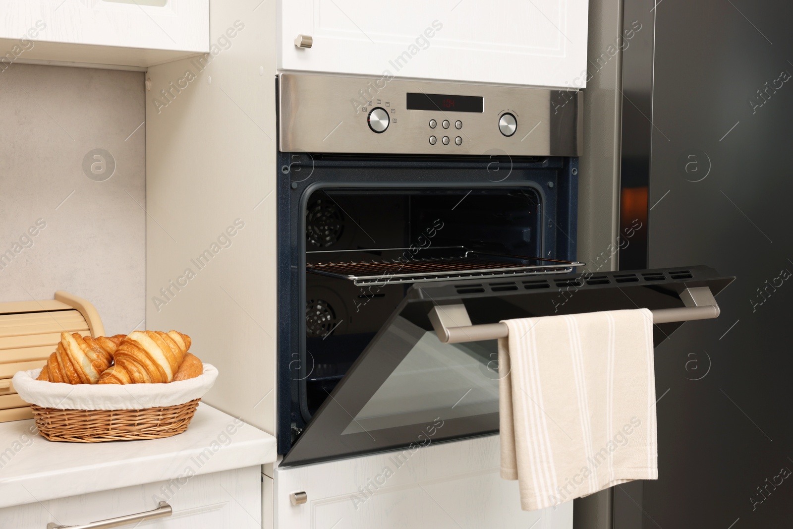 Photo of Open electric oven with towel and croissants in kitchen. Cooking appliance