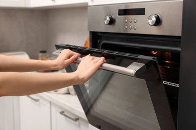 Photo of Woman using electric oven in kitchen, closeup