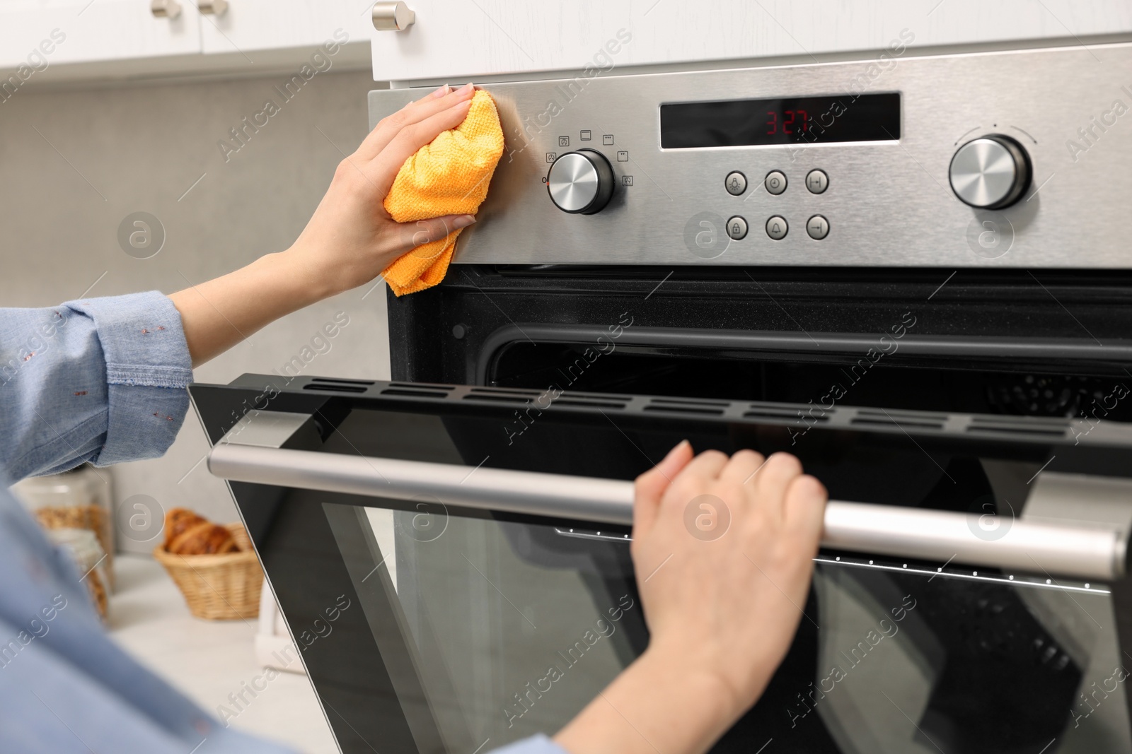 Photo of Woman cleaning electric oven with rag in kitchen, closeup