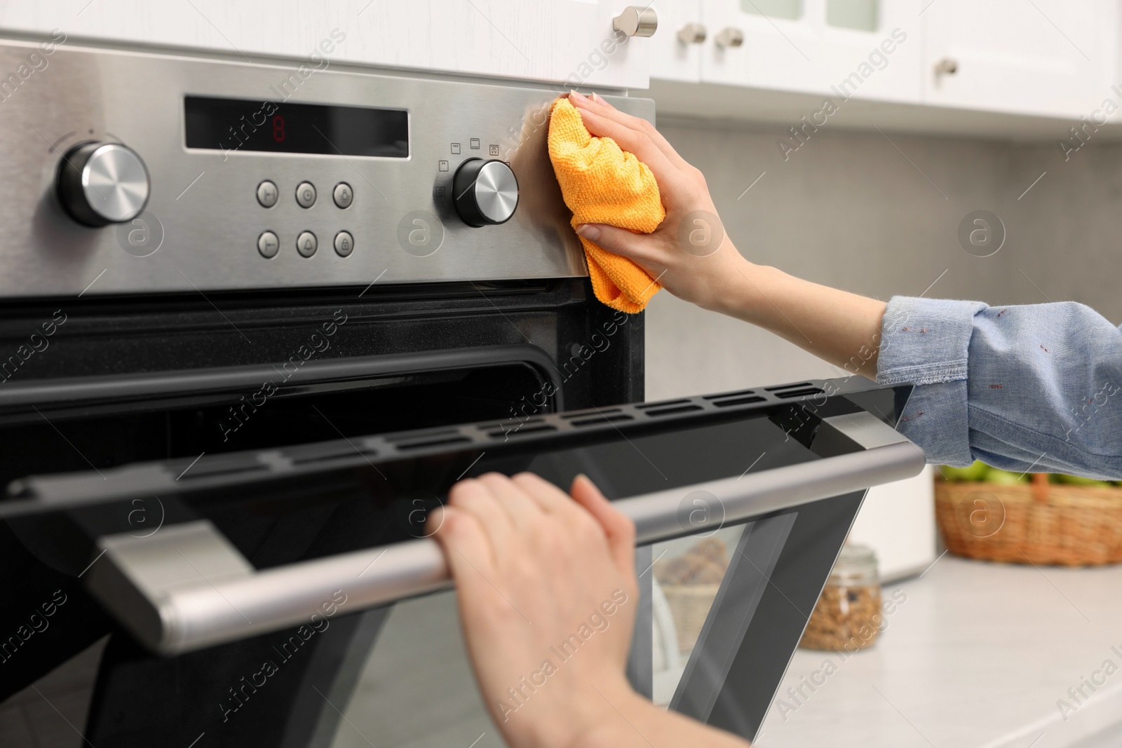 Photo of Woman cleaning electric oven with rag in kitchen, closeup