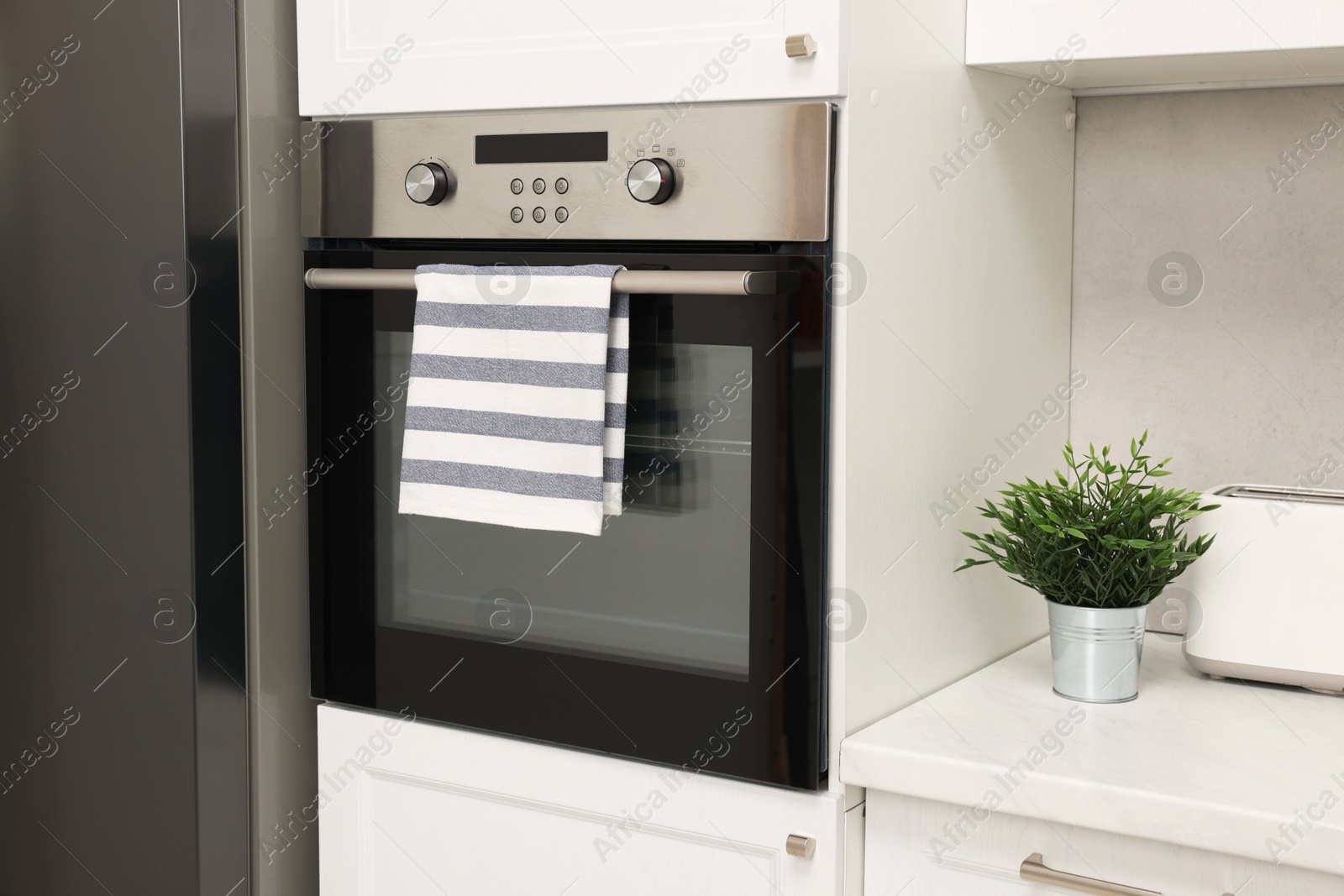 Photo of Electric oven with striped towel in kitchen. Cooking appliance