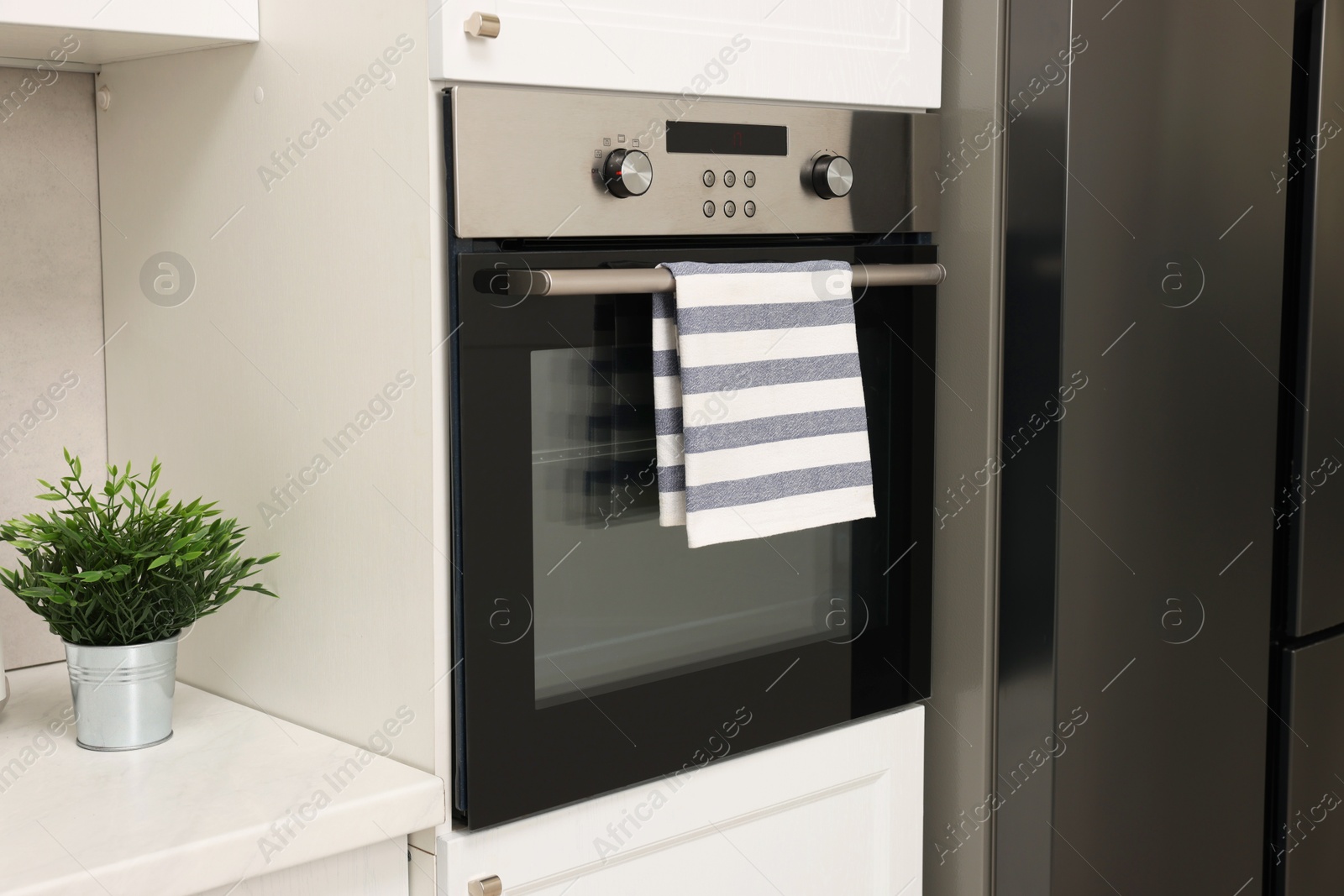 Photo of Electric oven with striped towel in kitchen. Cooking appliance