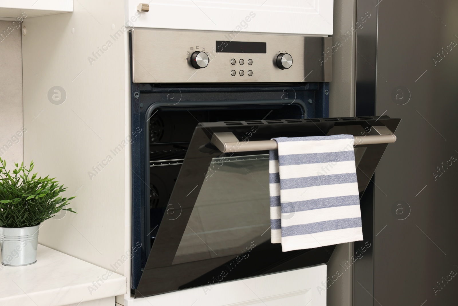 Photo of Open electric oven with striped towel in kitchen. Cooking appliance