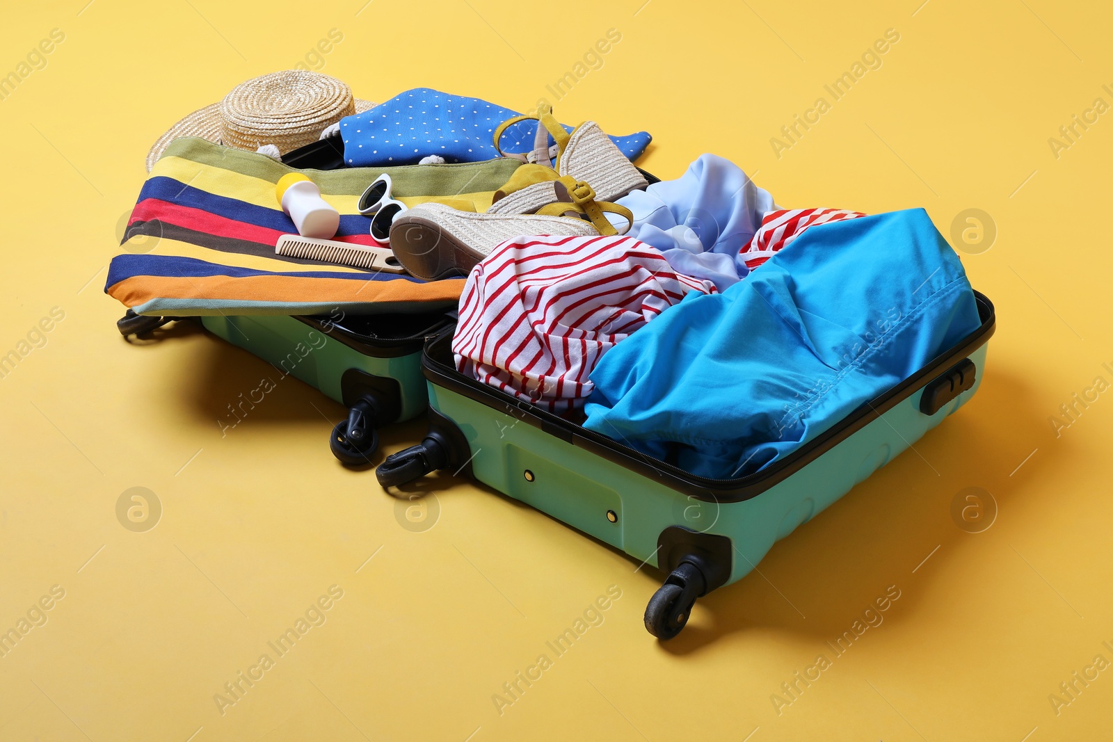 Photo of Open suitcase with traveler's belongings on yellow background