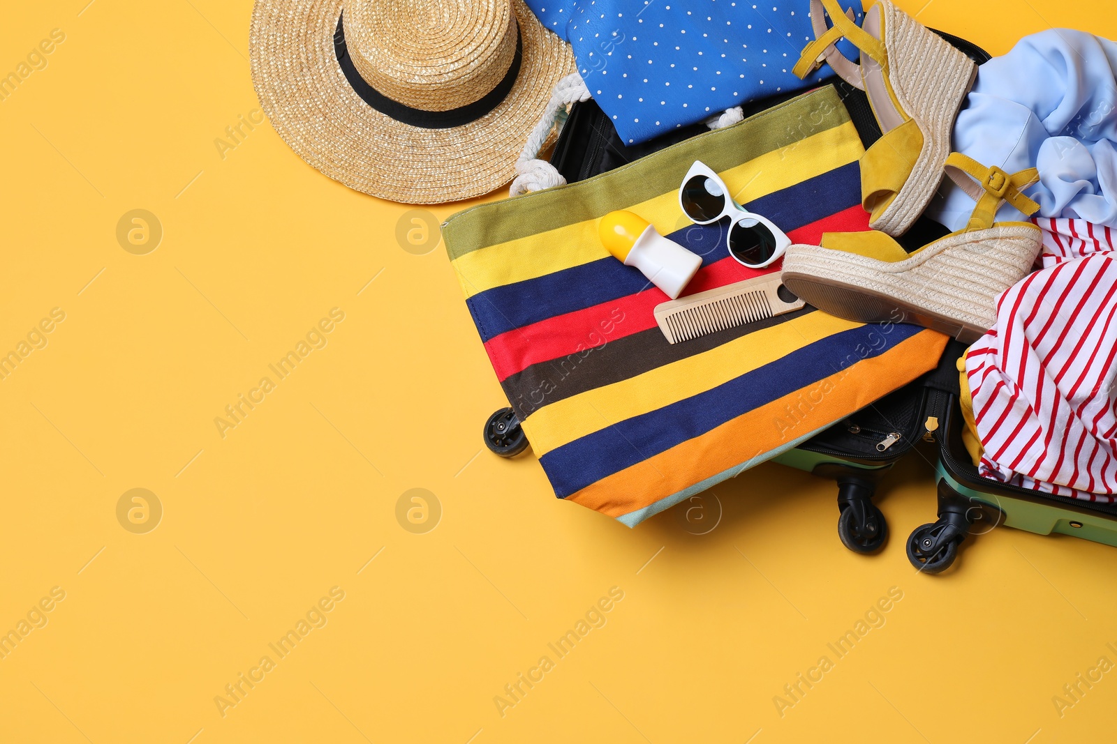 Photo of Open suitcase with traveler's belongings on yellow background, top view. Space for text