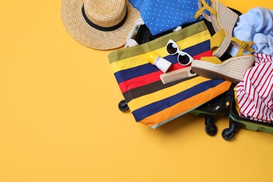 Open suitcase with traveler's belongings on yellow background, top view. Space for text