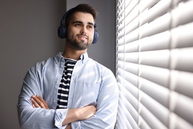 Photo of Man with headphones listening to music near window blinds at home, space for text