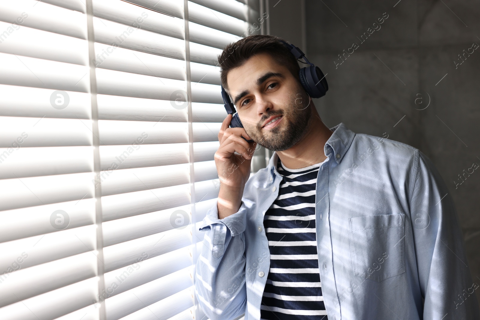 Photo of Man with headphones listening to music near window blinds at home, space for text