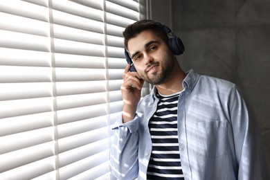 Photo of Man with headphones listening to music near window blinds at home, space for text