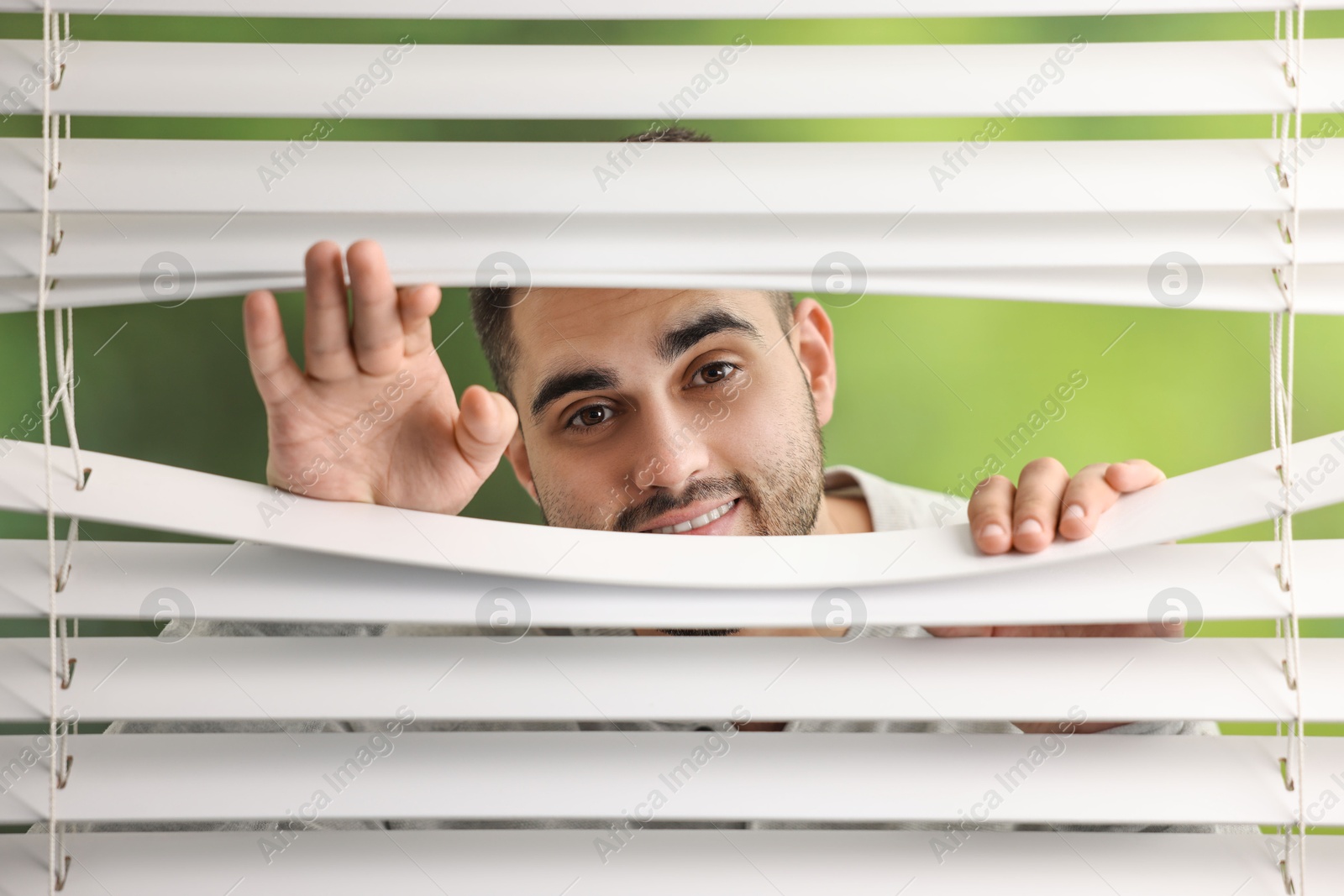 Photo of Young man looking through window blinds on blurred background