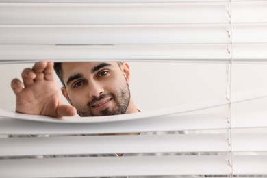 Photo of Young man looking through window blinds, space for text
