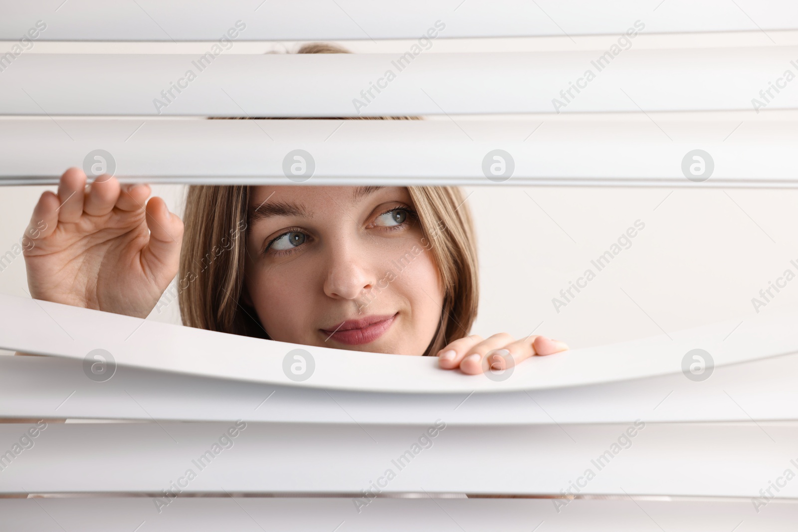 Photo of Young woman looking through window blinds on white background, space for text