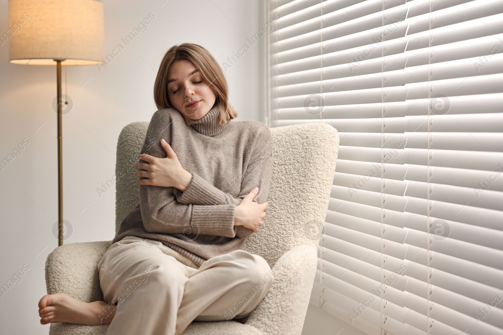 Photo of Woman sitting on armchair near window blinds at home, space for text