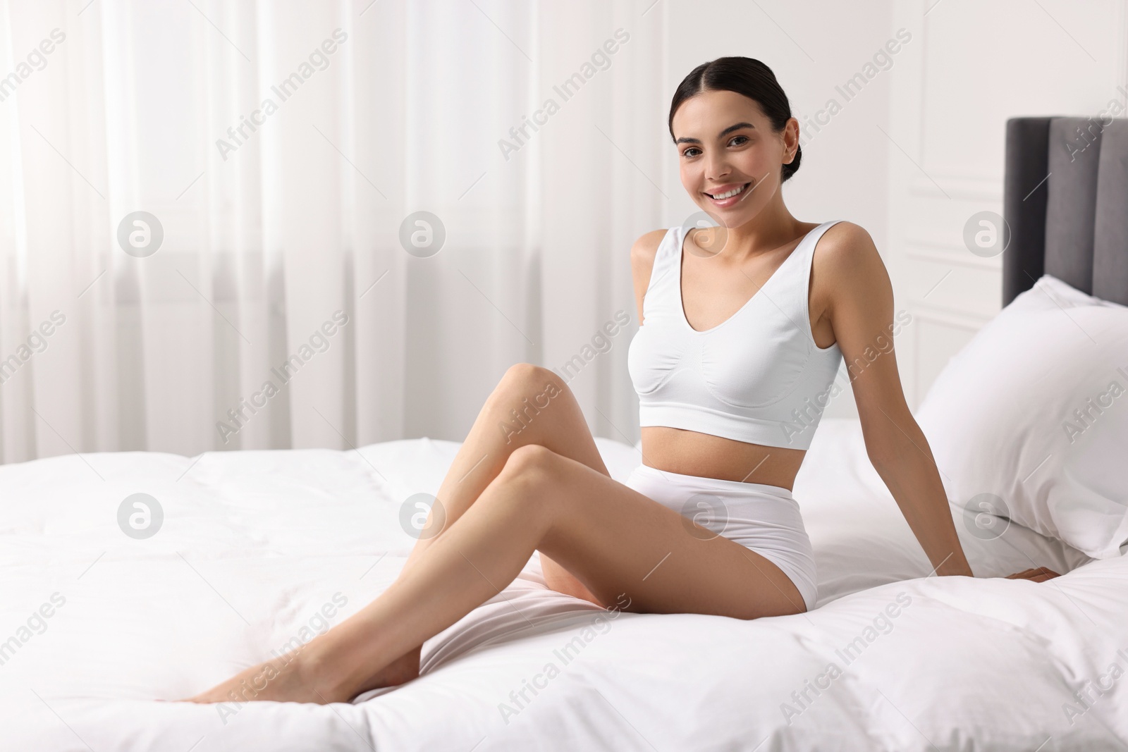 Photo of Smiling woman with perfect skin in underwear on bed, space for text. Body care