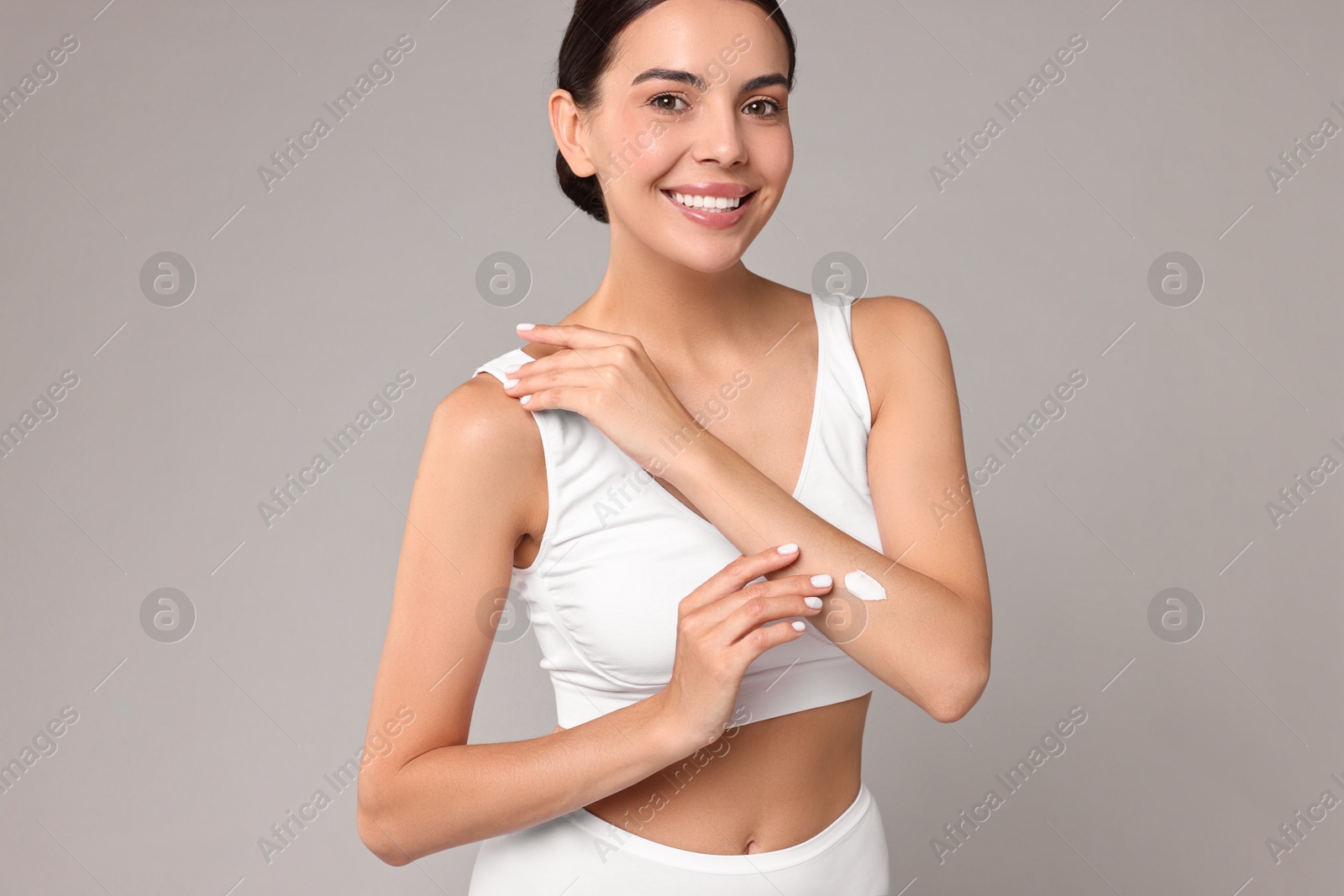 Photo of Smiling woman applying cream onto hand on grey background. Body care